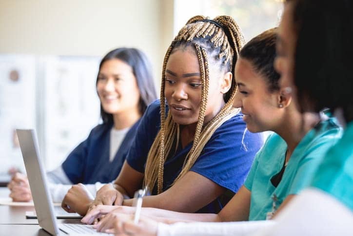 Four CNA students in a classroom with their laptops, learning to become nurses. 