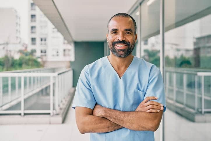 A male nurse with his arms crossed smiling for the camera. 