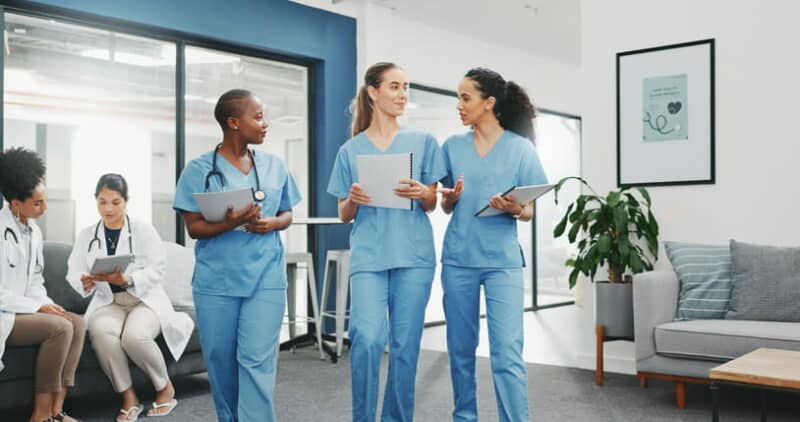Three nurses are walking and talking together at a skilled nursing facility.