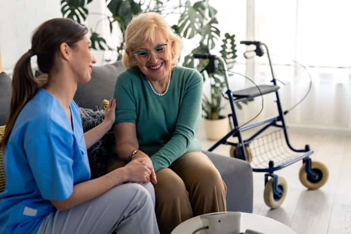 An aid sits with an elderly woman in an assisted living facility. 
