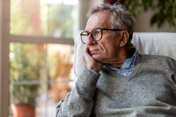 An Elderly Man Rests His Head In His Hand As He Looks Out The Window.