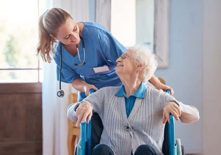 An elderly lady sits in a chair as she gazes out the window. 