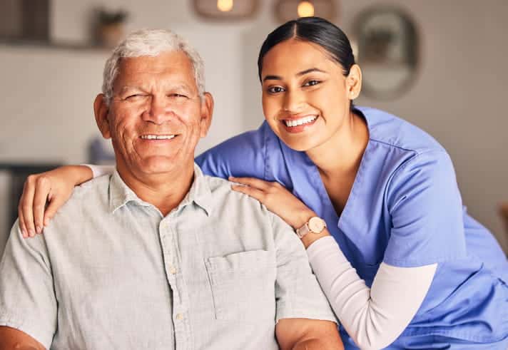 An assisted living facility aid posing with an elderly gentleman as they smile for a photo. 