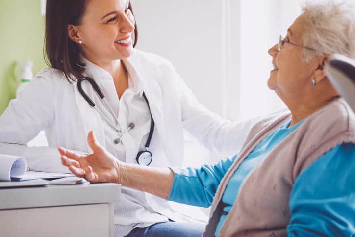 A doctor smiling as she speaks with her elderly patient.