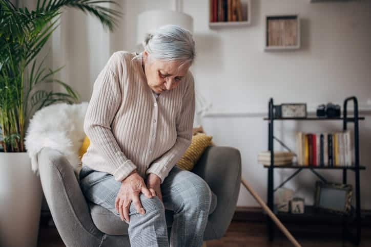 An elderly woman holding her knee if pain due to arthritis. 