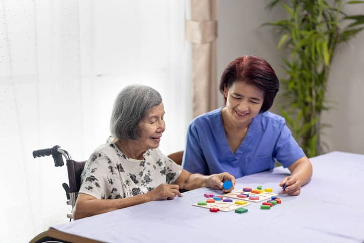 An aid assisting an Alzheimer's patient with a puzzle at a skilled nursing facility.