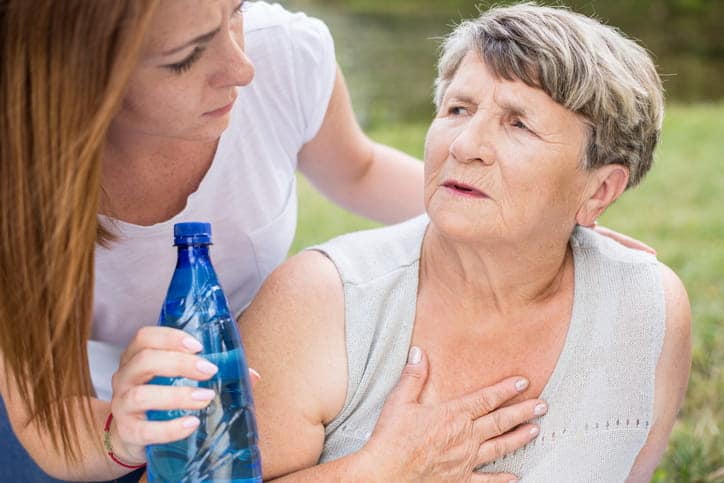 A Concerned Woman Is Offering Water To An Older Woman As They Sit Out In The Heat.