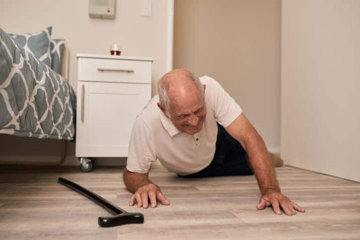 An Elderly Man On The Floor Next To His Cane After Falling Near His Bed. 
