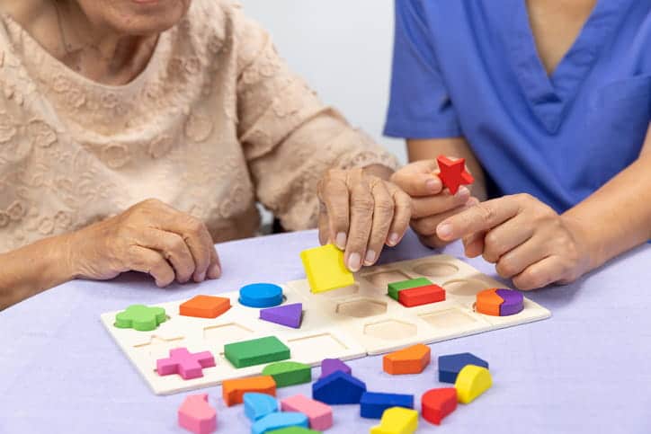 Benefits Of Memory Care In Arizona Assisted Living Facilities 1 An Assisted Living Facility Nurse Completes A Puzzle With A Memory Care Patient.