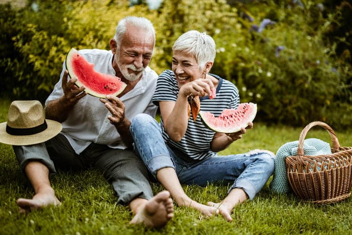 Two Seniors Eating Watermelon As They Have A Picnic In The Hot Weather. 