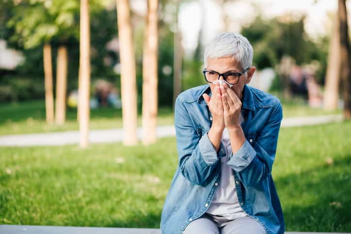 An Older Woman Blowing Her Nose While Being Outside Near Allergens.