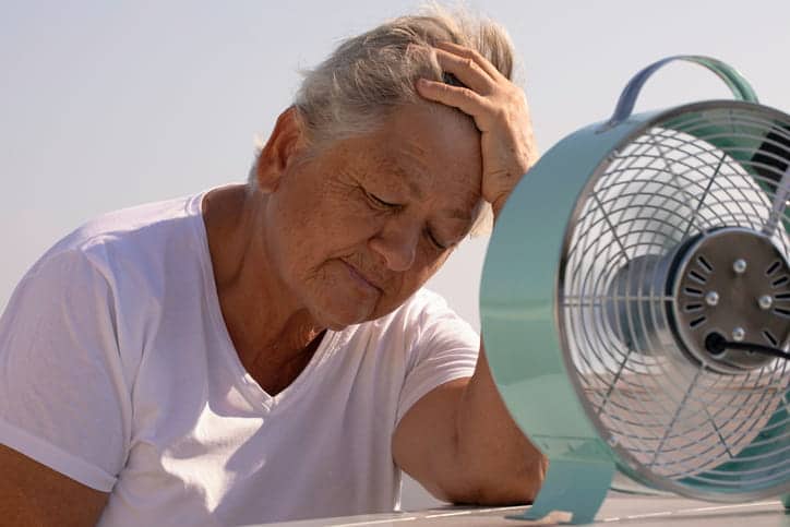 An Elderly Woman Sitting In Front Of A Fan.