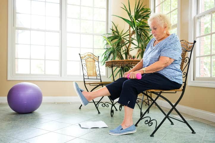 An Elderly Woman Performing Leg Exercises While Sitting In A Chair.