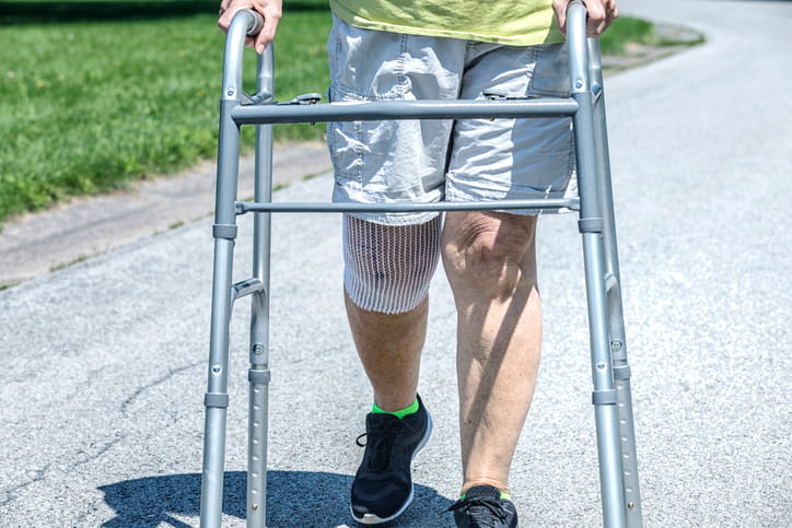 A Man Walking With A Walker After Knee Therapy.