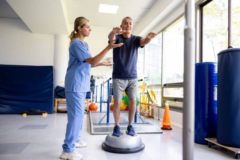How Physical Therapy For Fall Prevention Protects Your Safety 1 Mature Latin American Man Doing Exercises Using A Balance Ball With The Help Of His Physical Therapist