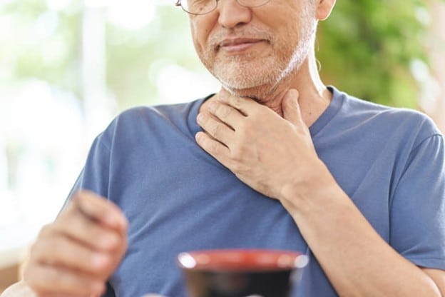 An Elderly Man Holds His Throat Due To Dysphagia Symptoms.