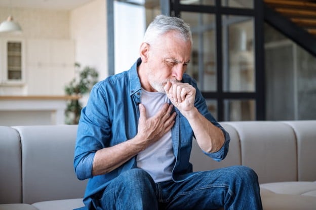 An Elderly Man Holds His Chest As He Coughs Due To Shortness Of Breath.