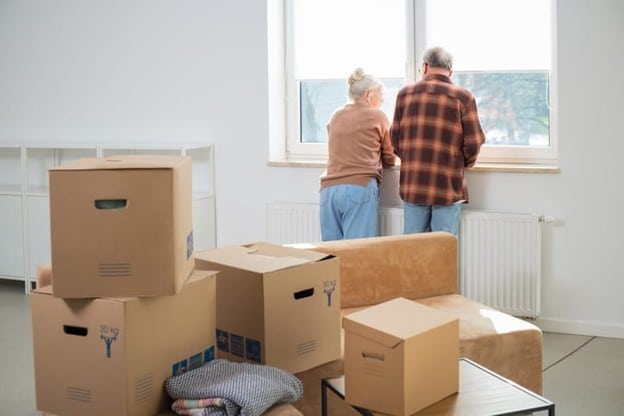 Two Seniors Look Out The Window As Their Livingroom Is Boxed Up Before They Move.