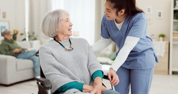 A Nurse Assists A Patient In A Skilled Nursing Care Facility.