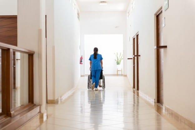 A Skilled Nursing Facility Nurse Pushes A Patient In A Wheelchair.